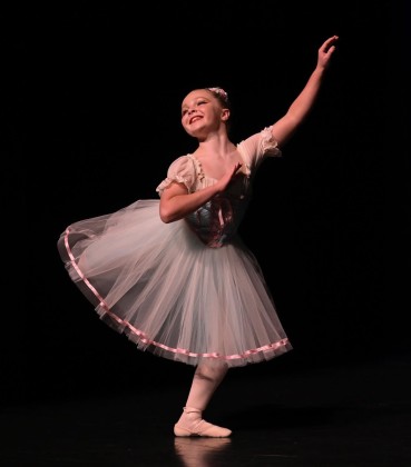 A student from Simone's School of Performing Arts dances on stage, embodying the joy of movement and love for dance. Discover how our classes instill a passion for dance in kids. Keywords: kids dance classes, Simone's School of Performing Arts, joy of movement, love for dance, creative classes.